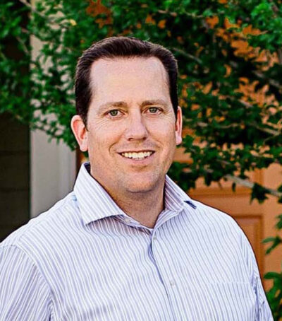 A man in a striped shirt standing next to a tree.