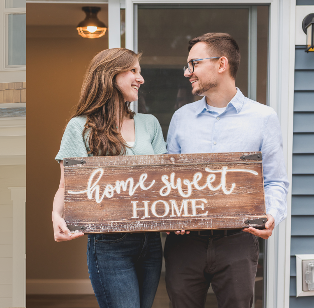 A man and woman holding up a sign that says " home sweet home ".