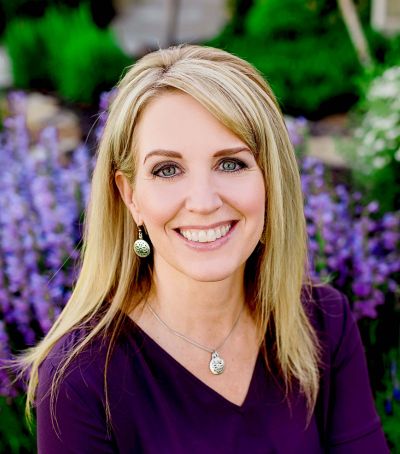 A woman in purple shirt standing next to flowers.